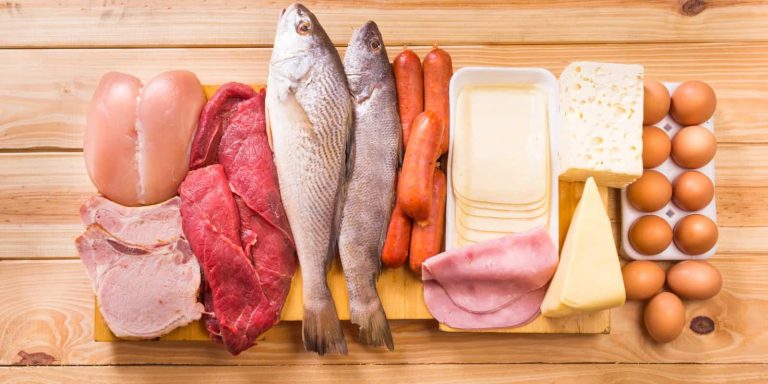 A selection of meat, fish, cheese, and eggs displayed on a wooden table