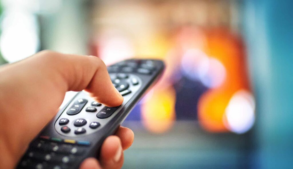 A person holding a TV remote with a blurred TV in the background