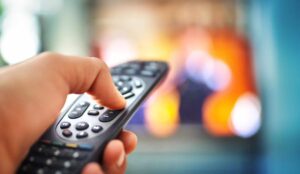 A person holding a TV remote with a blurred TV in the background