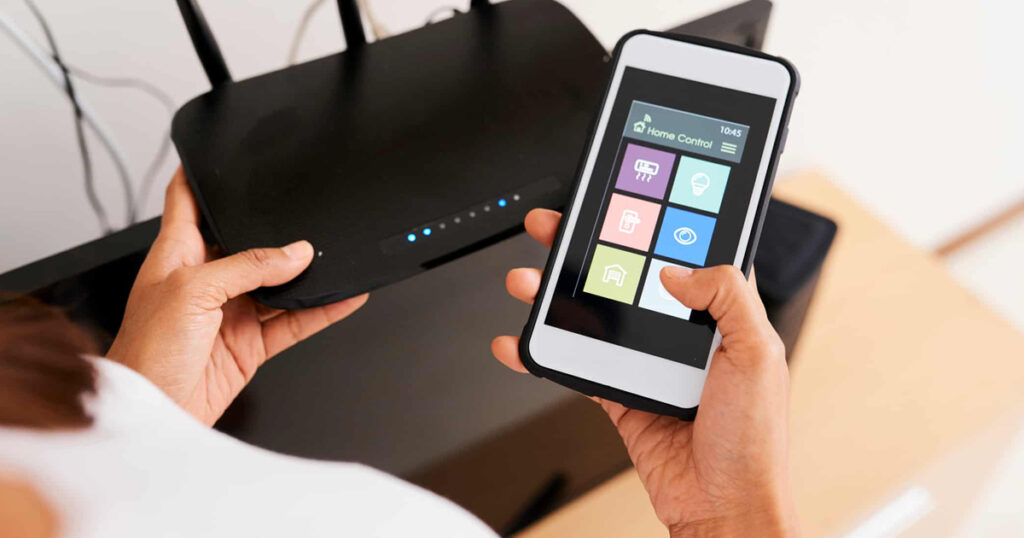 An individual looking down at a WiFI router in one hand and a cell phone in the other