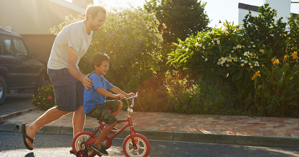 Man alongside boy riding bike through a neighborhood